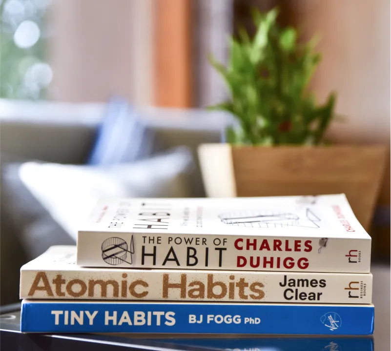 Stack of books on habits next to a plant
